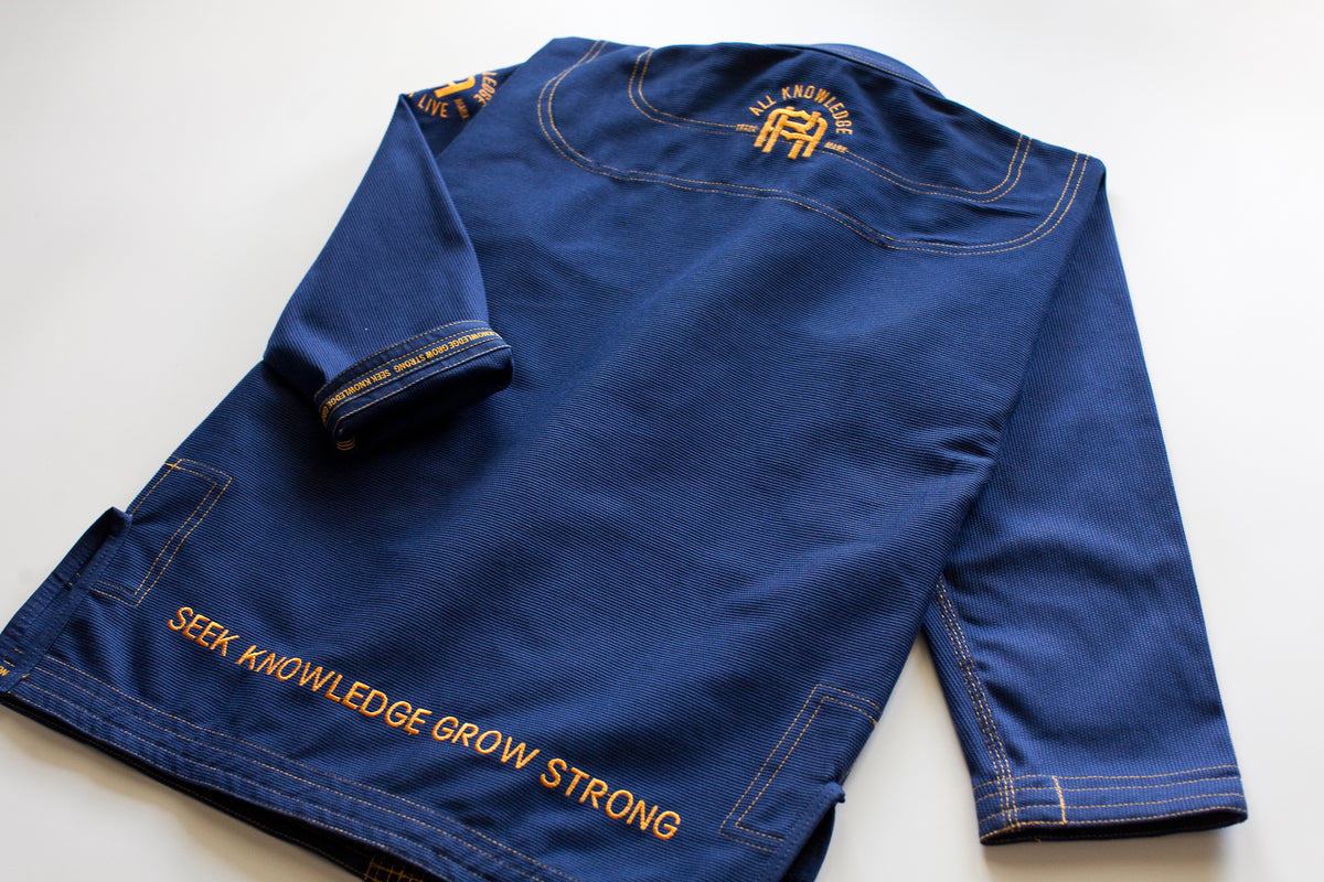 All Knowledge blue Brazilian Jiu-Jitsu Gi with gold stitching, embroidered AK logos, Seek Risk Live sleeve design, matching pants, and branded patches, displayed flat on a white background.