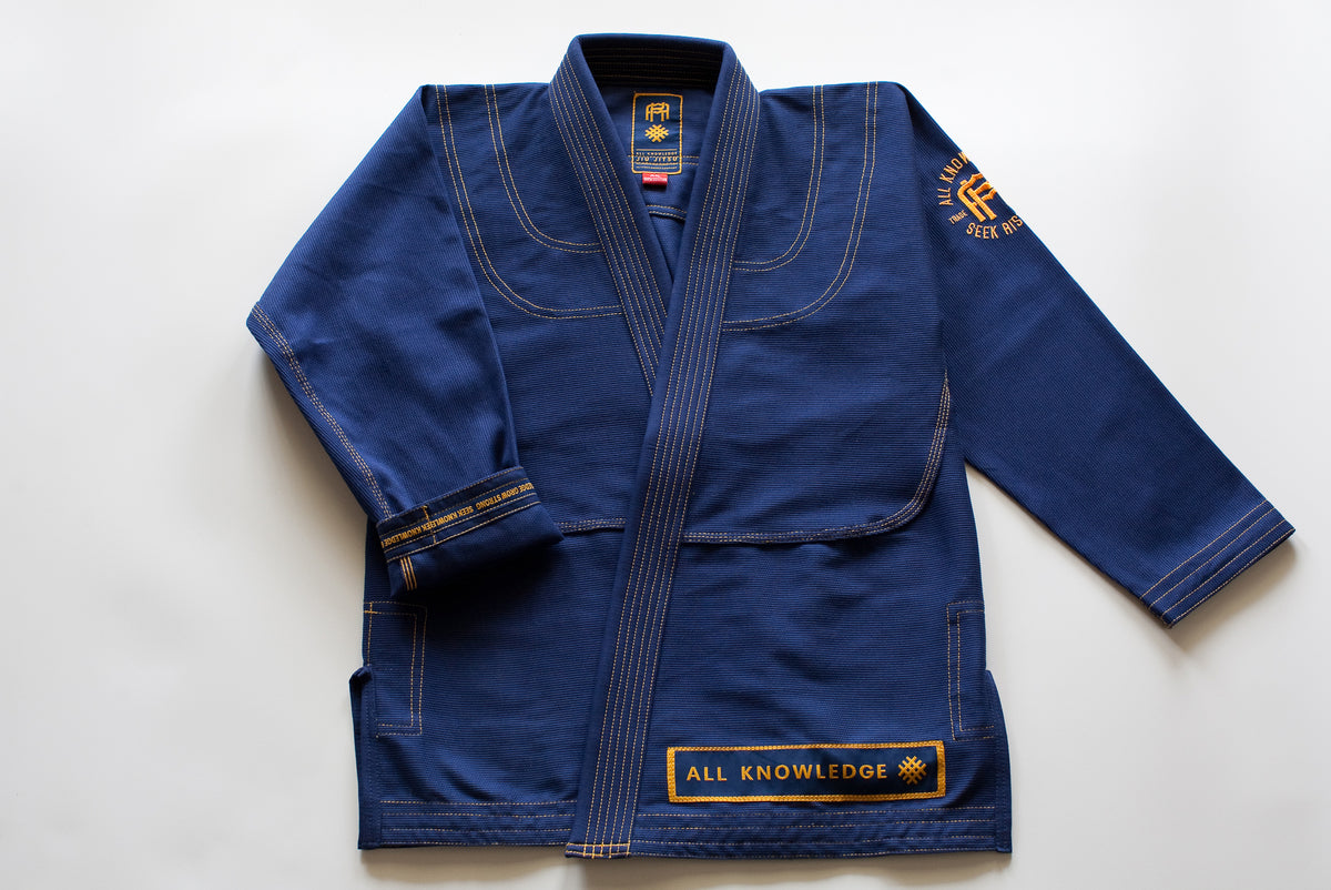 All Knowledge blue Brazilian Jiu-Jitsu Gi with gold stitching, embroidered AK logos, Seek Risk Live sleeve design, matching pants, and branded patches, displayed flat on a white background.